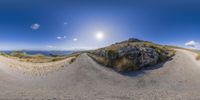 a fisheye lens image of a dirt road with mountains in the background and clouds in the sky