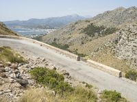 there is a person standing on the road by the water and mountains behind them with a vehicle on the road