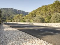 a paved highway is surrounded by rocks and forest on a sunny day from the side