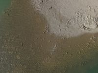 an aerial view of a boat docked on the beach with rocks in sand and water