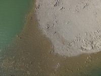 an aerial view of a boat docked on the beach with rocks in sand and water