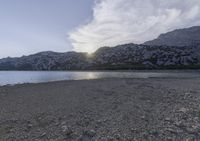 a horse is sitting in the sand by water and mountains in a blue sky and white clouds