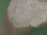 an aerial view of people walking next to a rock formation in the water on a beach