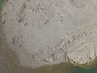 an aerial view of people walking next to a rock formation in the water on a beach