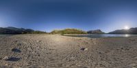 this is an image of a wide angle panorama of a beach and mountains with a blue sky