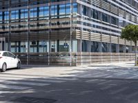 a white car parked in front of a tall building with several windows and one car is near it