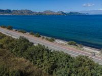 a highway that is going over some water and hills in the distance are trees and the ocean