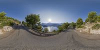 360 - angle photo taken from the road in front of a lake and trees with water in the background