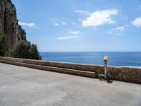 a paved road is next to the shore with a stone fence and a large cliff