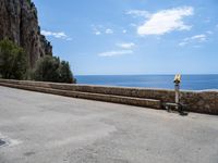 a paved road is next to the shore with a stone fence and a large cliff