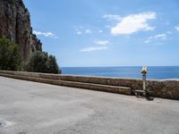 a paved road is next to the shore with a stone fence and a large cliff