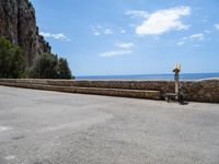 a paved road is next to the shore with a stone fence and a large cliff