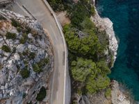 aerial view of a car on the side of road by a river below trees on a cliff