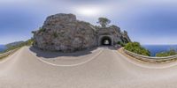 a view from a fish eye lens of a road going through a tunnel under a cliff