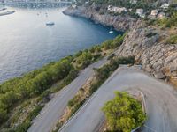 an empty paved road between two mountains near the water's edge, with boat and boat in distance