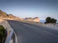 a car drives along the empty road in front of the ocean and rocky mountains at the edge