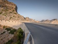 a car drives along the empty road in front of the ocean and rocky mountains at the edge