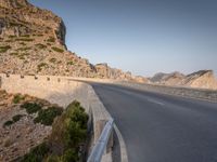 a car drives along the empty road in front of the ocean and rocky mountains at the edge