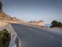 a car drives along the empty road in front of the ocean and rocky mountains at the edge