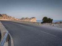 a car drives along the empty road in front of the ocean and rocky mountains at the edge