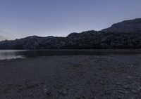 the person is walking next to the water at dusk on the shore in the mountains