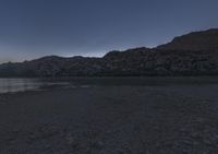 the person is walking next to the water at dusk on the shore in the mountains