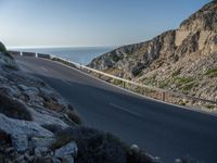 a person riding a bike down a road by the water and cliff side, looking back