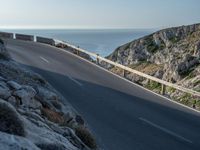 a person riding a bike down a road by the water and cliff side, looking back