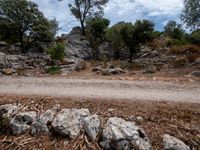 a motorcycle riding past some large rocks near trees and dirt road as people walk by