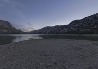 a lake with a boat on it in the distance at dusk over the mountains and sand