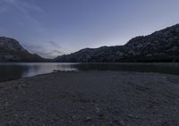 a lake with a boat on it in the distance at dusk over the mountains and sand