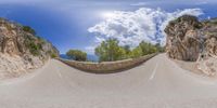 the sky is blue and very cloudy as a road bends in half, making it look like it is going up