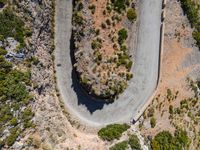 the aerial view of a road running on the side of a mountain, with bushes growing near a curve