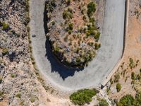 the aerial view of a road running on the side of a mountain, with bushes growing near a curve