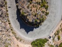 the aerial view of a road running on the side of a mountain, with bushes growing near a curve