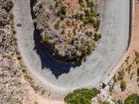 the aerial view of a road running on the side of a mountain, with bushes growing near a curve