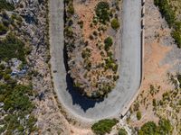 the aerial view of a road running on the side of a mountain, with bushes growing near a curve