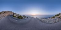 a road going down to the ocean from a cliff overlooking a sunrise and its reflection