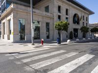 the empty street in front of a white building with an odd entrance to it is almost crosswalking