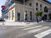 the empty street in front of a white building with an odd entrance to it is almost crosswalking