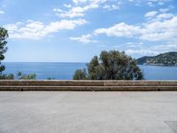 the view of the ocean from a stone bench at a seaside clifftop location under a cloudy blue sky