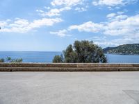 the view of the ocean from a stone bench at a seaside clifftop location under a cloudy blue sky