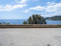 the view of the ocean from a stone bench at a seaside clifftop location under a cloudy blue sky