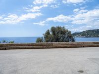 the view of the ocean from a stone bench at a seaside clifftop location under a cloudy blue sky