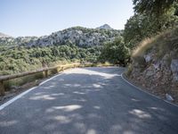 a bend in the road next to a mountain with green trees around it and some stone