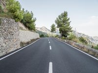 a winding road in the mountains surrounded by trees and boulders, with a mountain backdrop