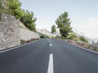 a winding road in the mountains surrounded by trees and boulders, with a mountain backdrop