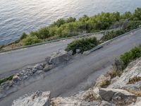 a person rides on the back of a motorcycle by a cliff overlooking the water and trees