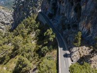 an aerial view of a scenic road between cliffs and trees with a road ahead of the camera