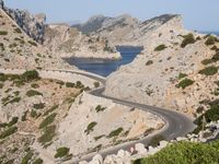 two vehicles driving on the narrow highway in front of the ocean near a cliff formation